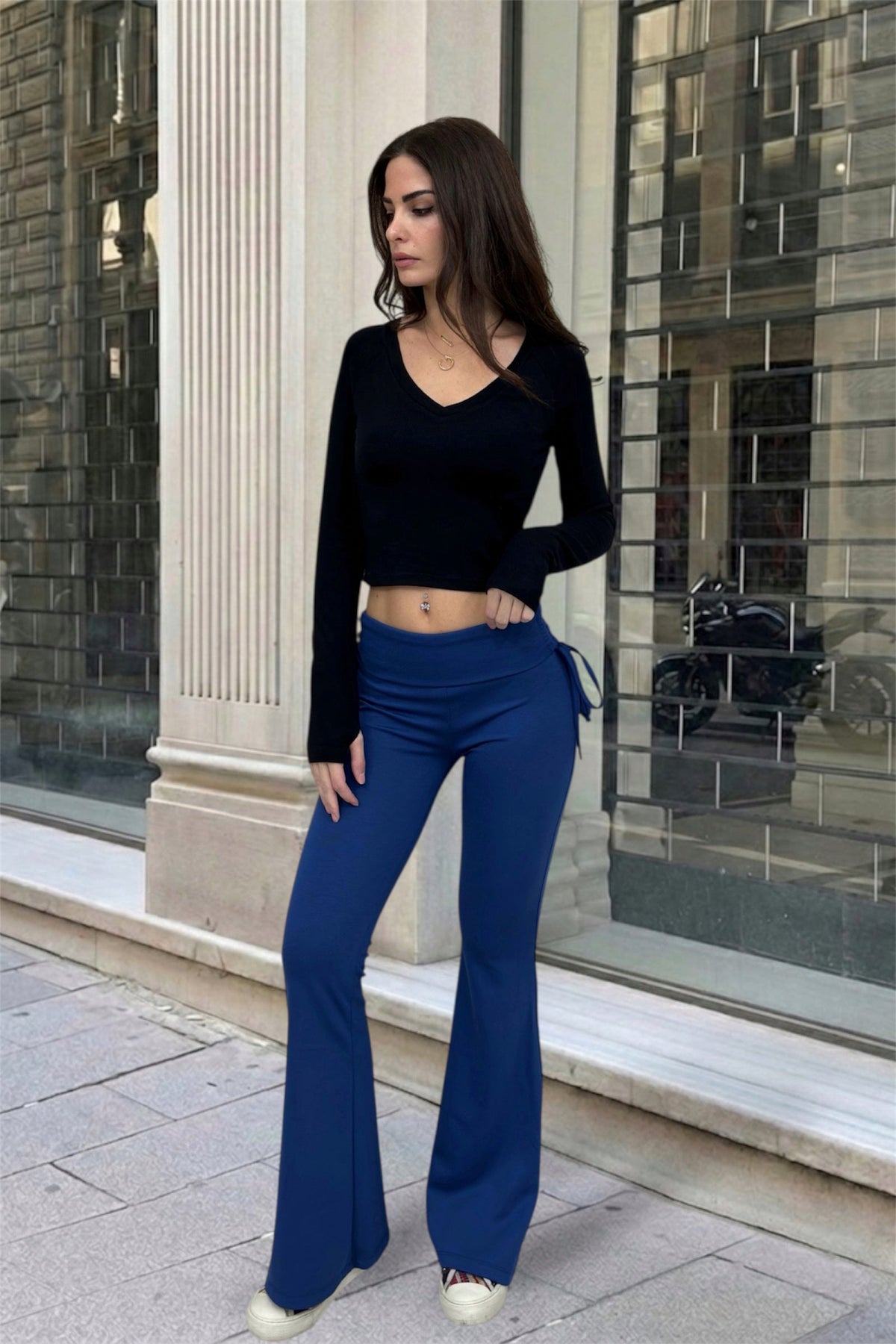 Woman wearing a black top and blue pants standing in front of a building.
