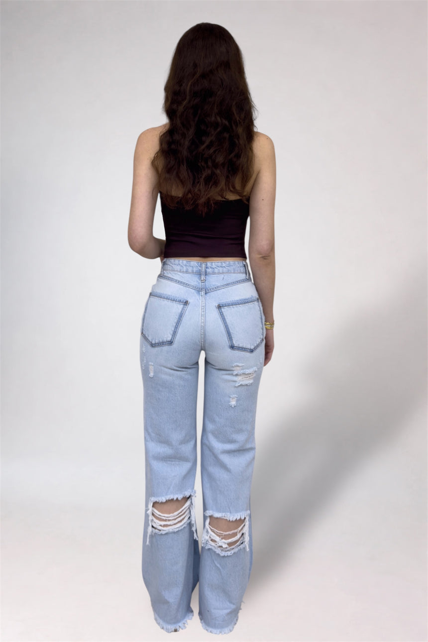 Person wearing light blue distressed jeans and a black top on a plain background