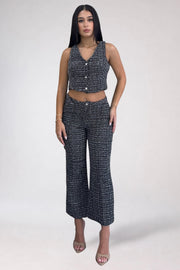 A woman modeling a matching sleeveless cropped top and wide-leg pants set in a black and white textured tweed fabric, photographed against a plain light gray studio background.
