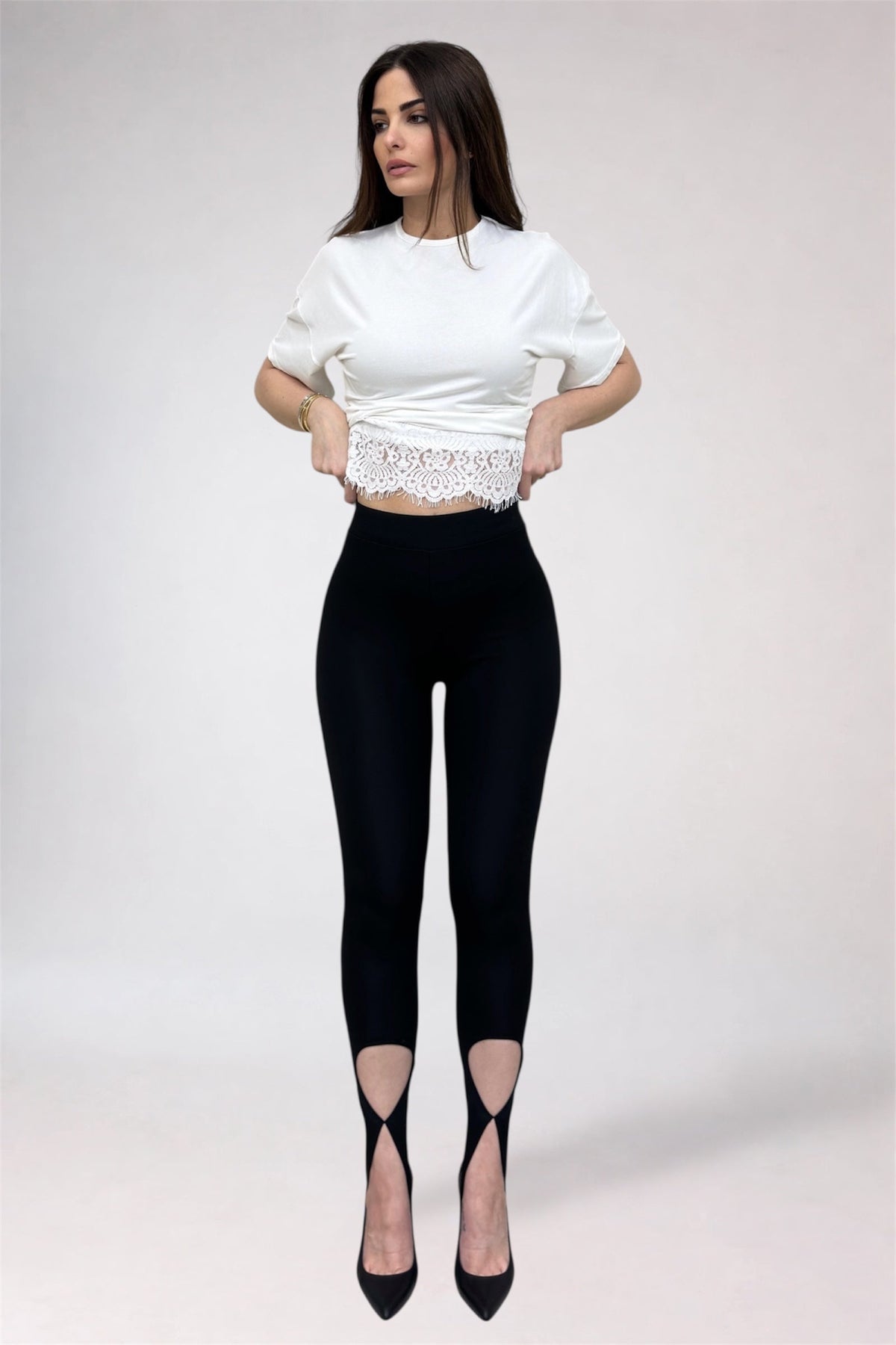 Woman wearing a white cropped top and black leggings with cut-out design on a plain background