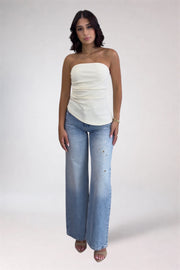 Woman wearing a white strapless top and blue jeans on a plain background