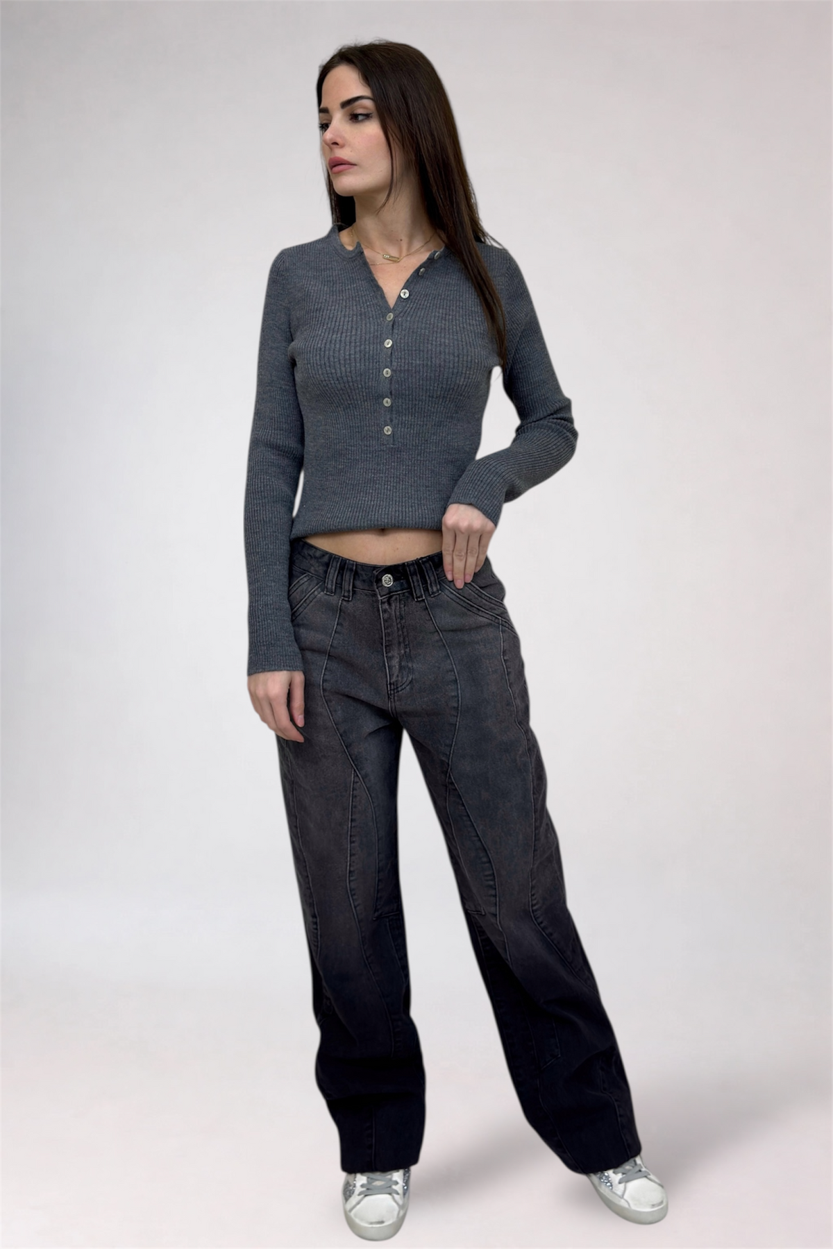 Woman wearing a gray long-sleeve top and black jeans on a white background
