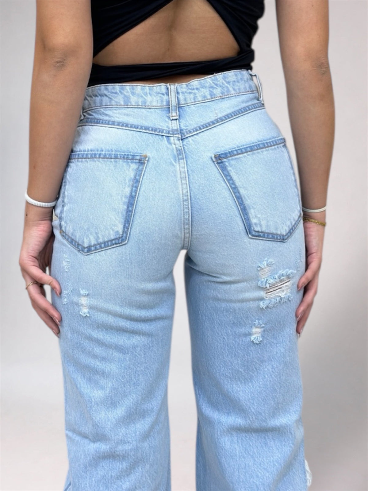 Light blue jeans with distressed details worn by a person on a plain background