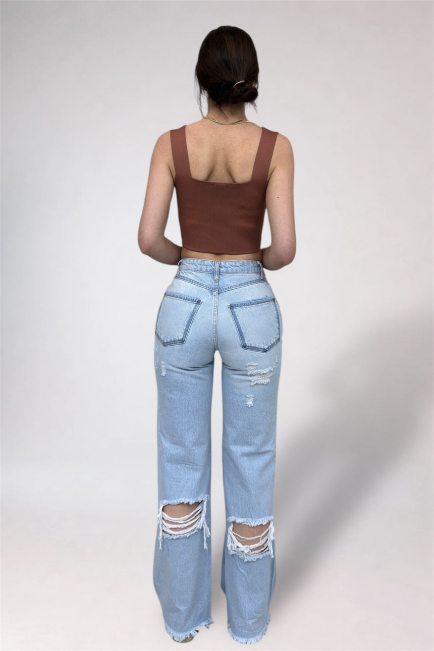 Person wearing a brown tank top and light blue ripped jeans on a white background