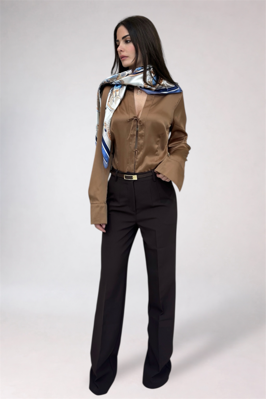 Woman wearing a brown satin shirt and black pants with a patterned scarf on a white background