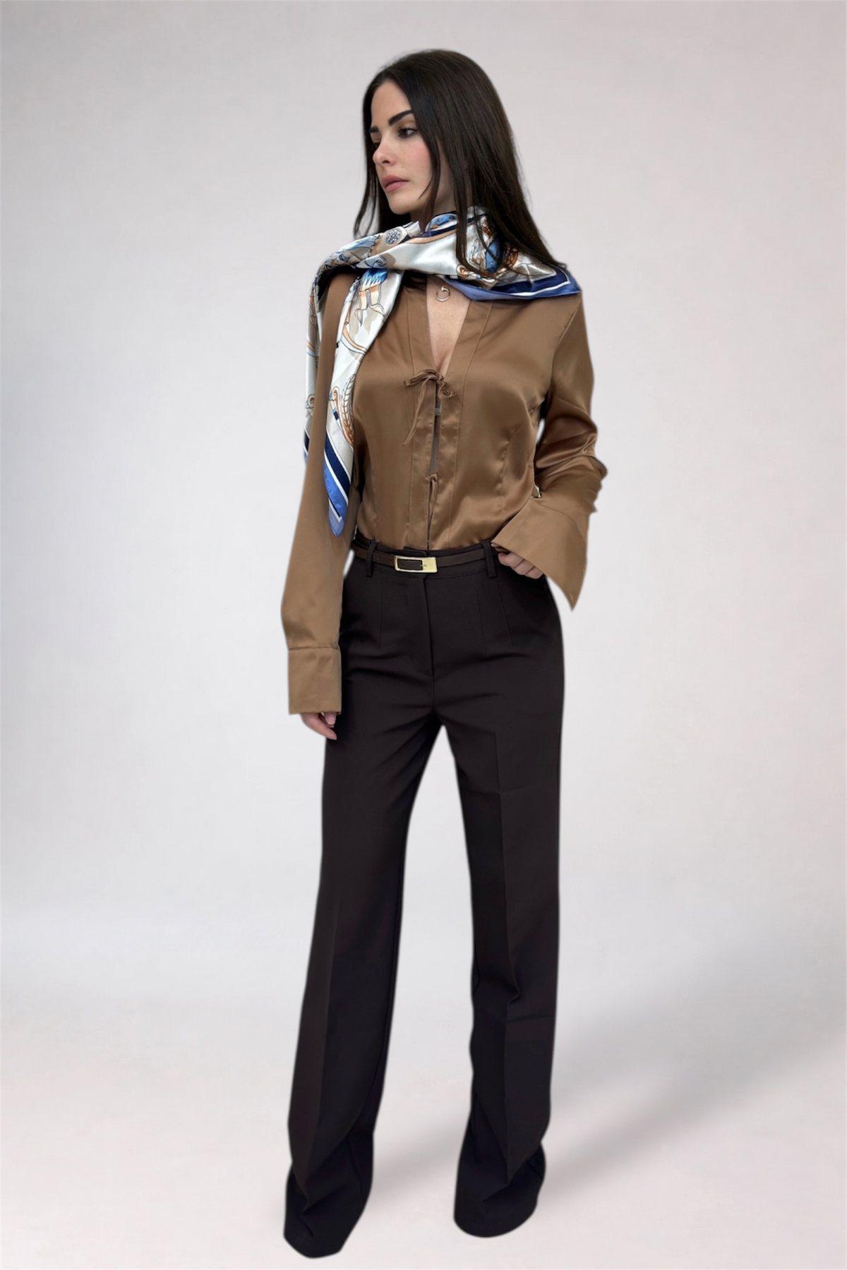 Woman wearing a brown shirt and black pants with a patterned scarf on a white background