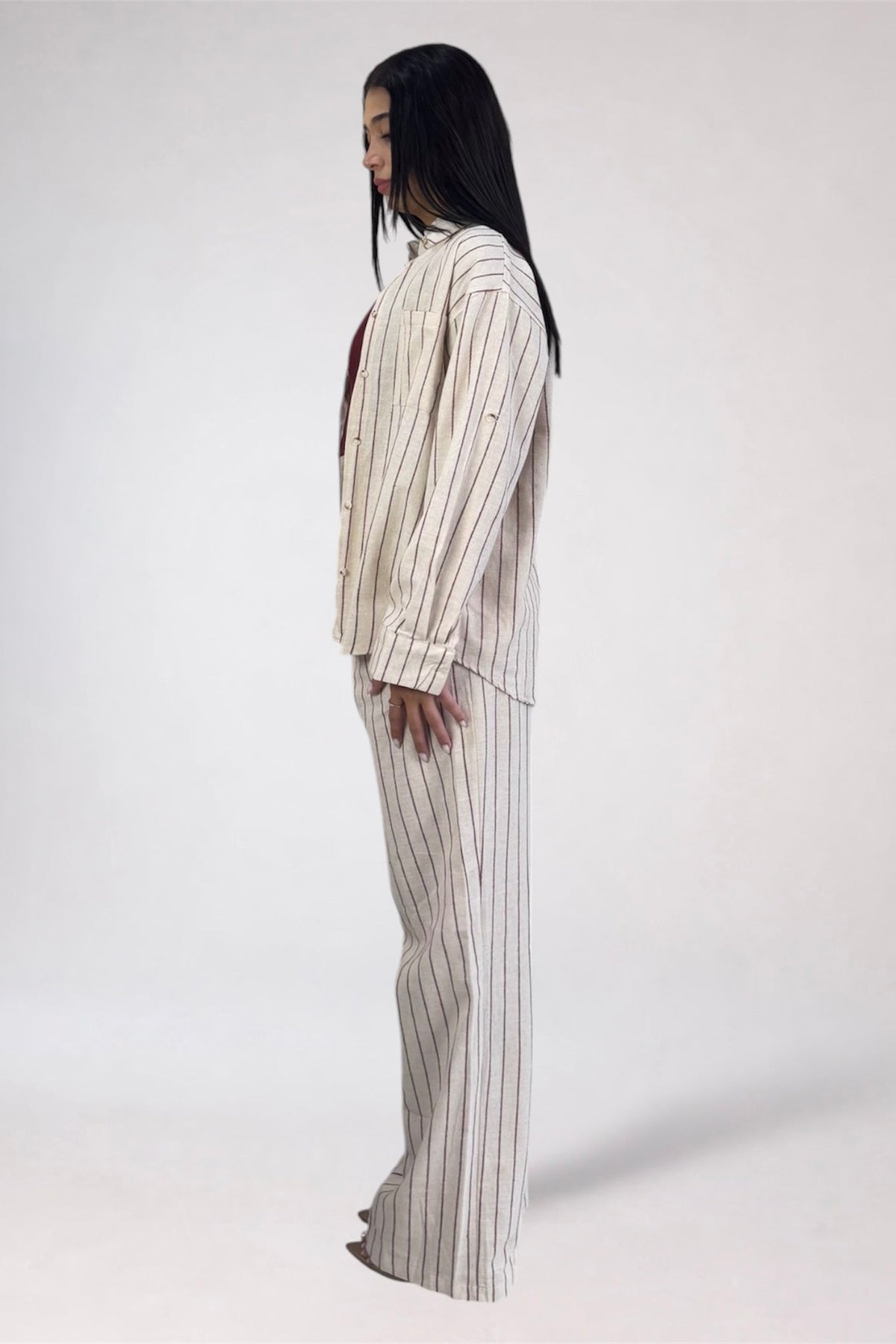A model shown from the side profile wearing a matching two-piece pinstripe lounge set in cream and beige with thin dark vertical stripes, photographed against a plain light gray studio background.