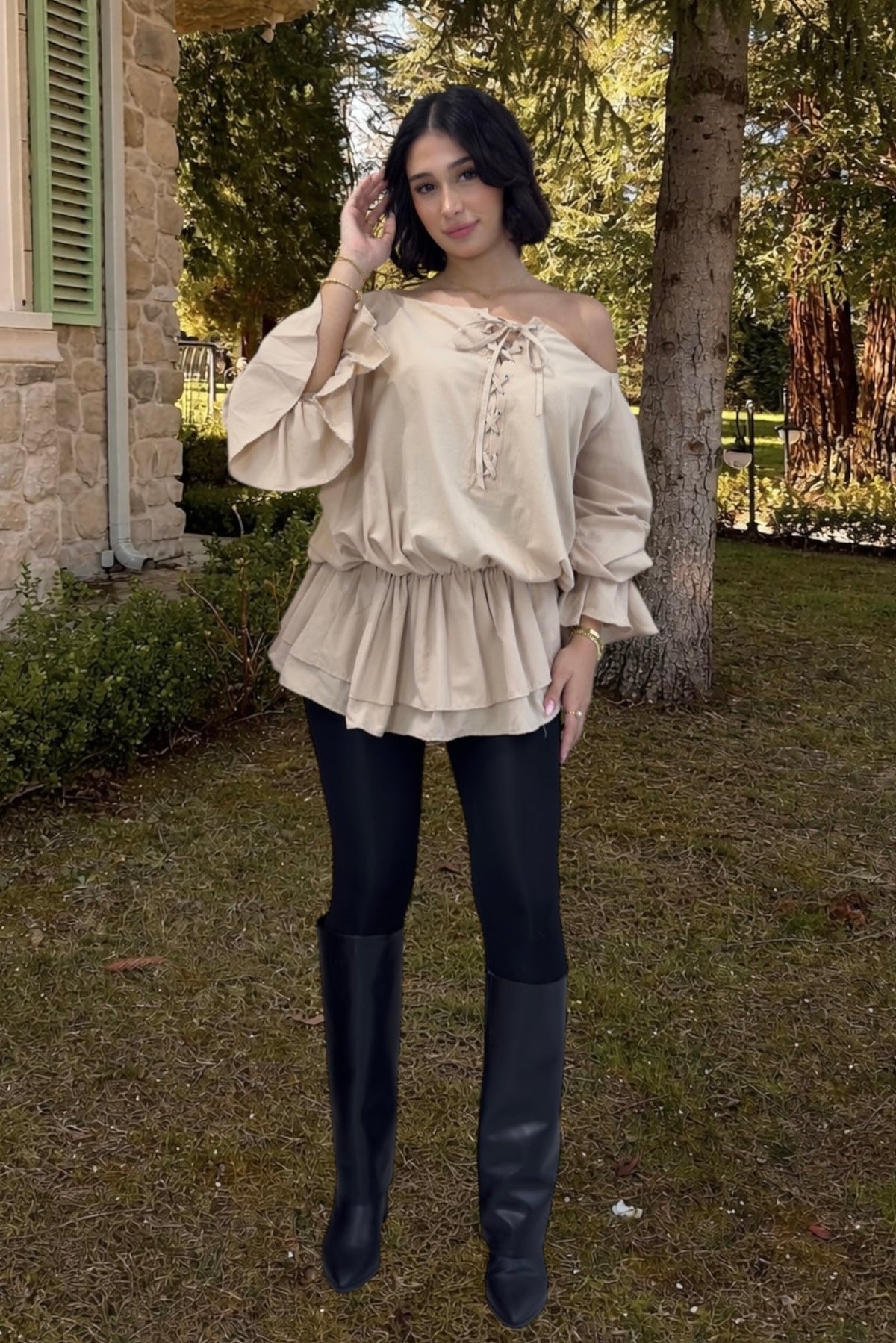 Woman wearing a beige off-shoulder blouse and black leggings outdoors.