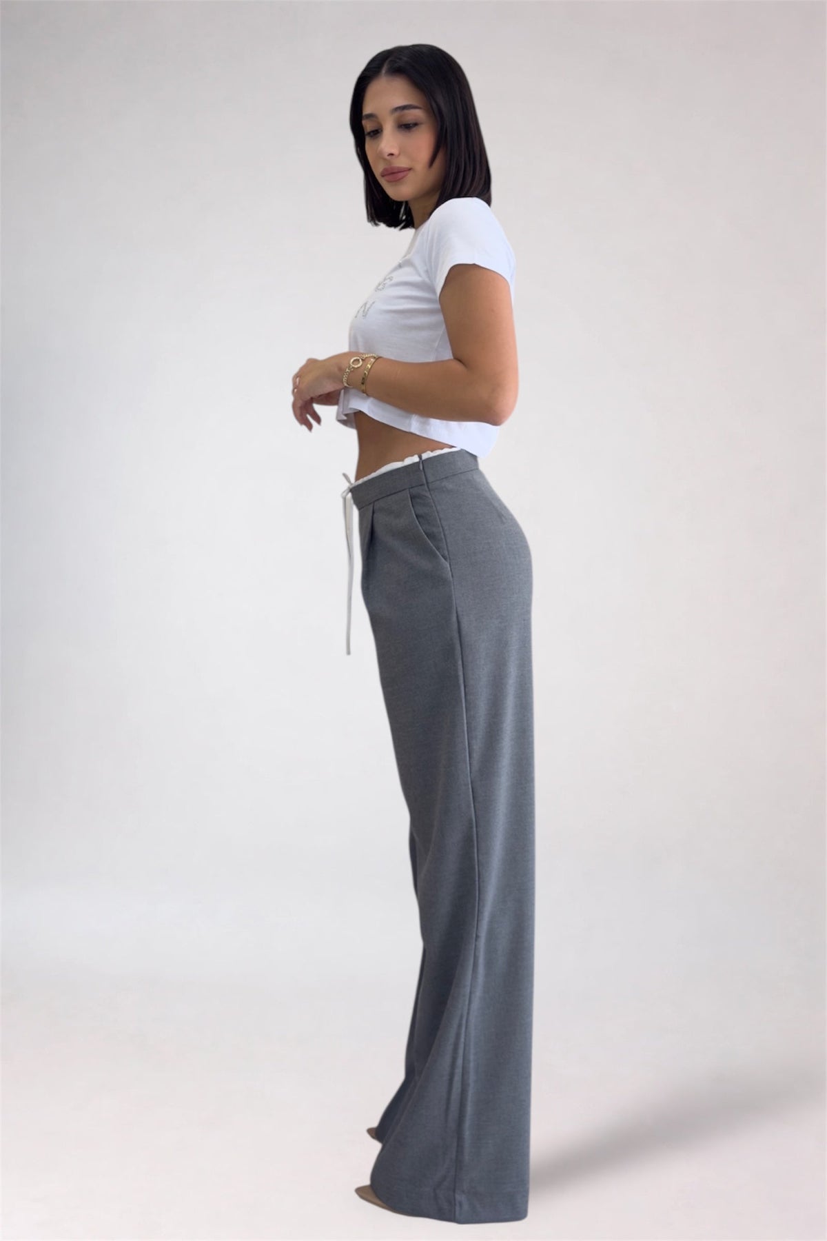 Woman wearing a white crop top and gray wide-leg pants on a plain background