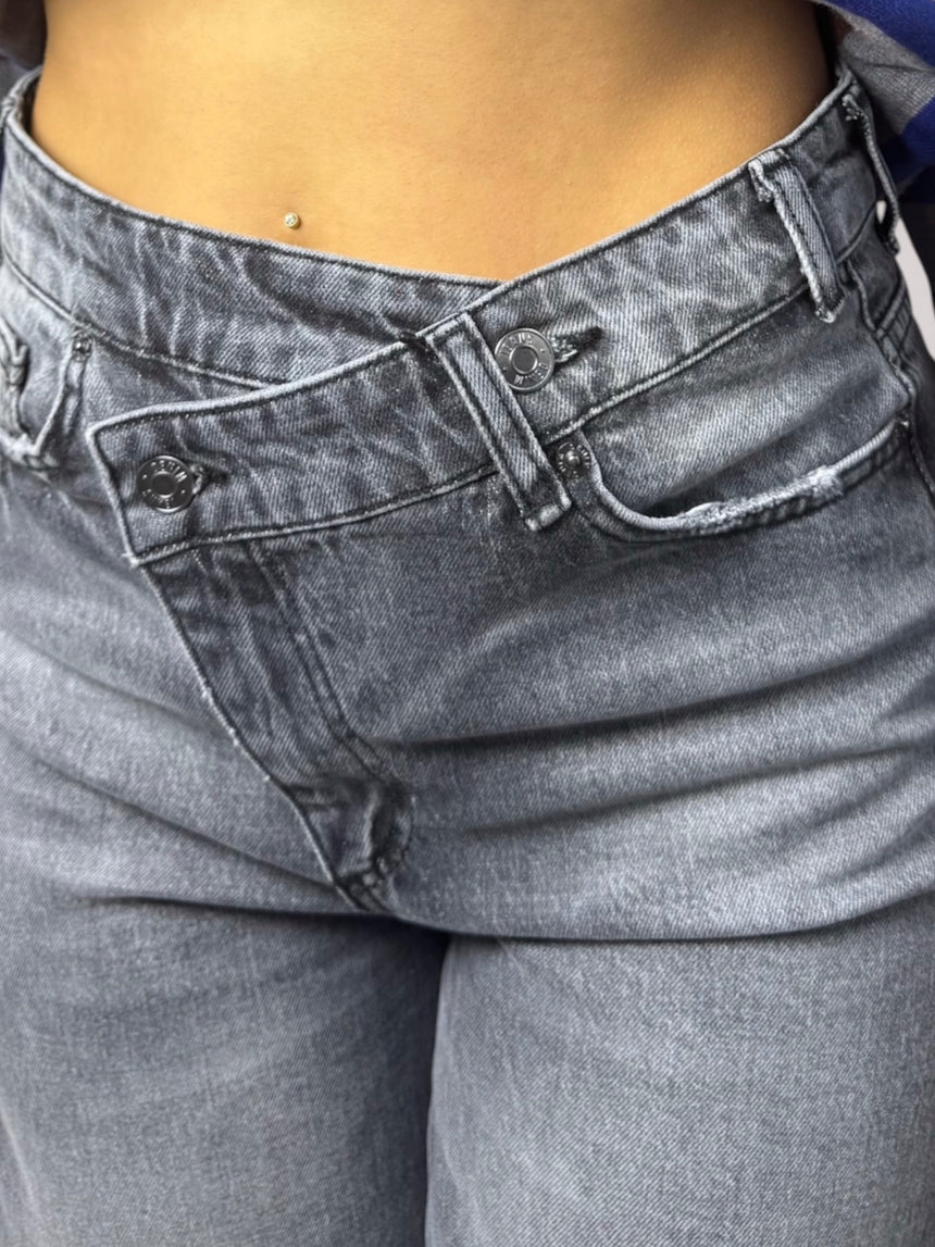 Close-up of a person wearing gray washed denim jeans, showing the front waistband, button, belt loops, and pocket details.