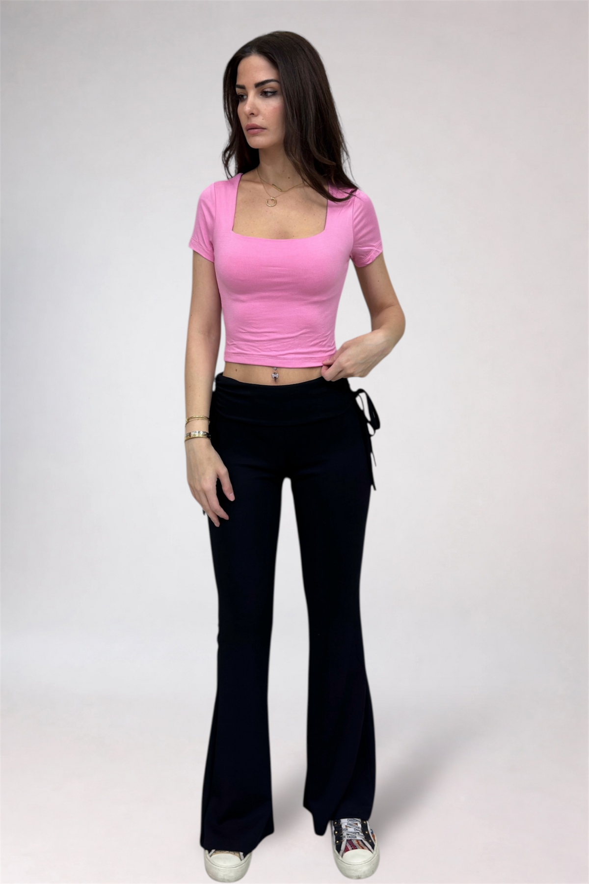 Woman wearing a pink top and black pants on a white background