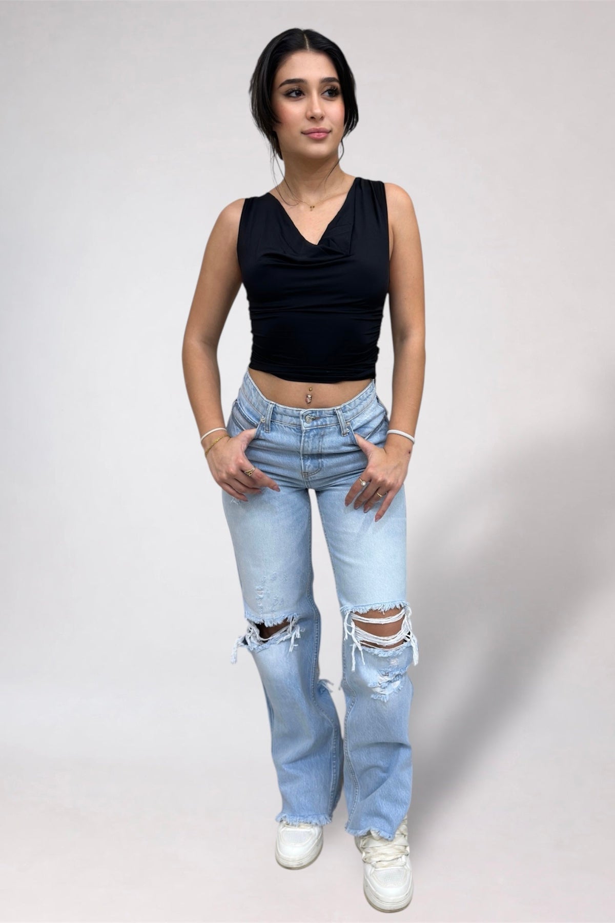 Woman wearing a black sleeveless top and light blue jeans with a white background