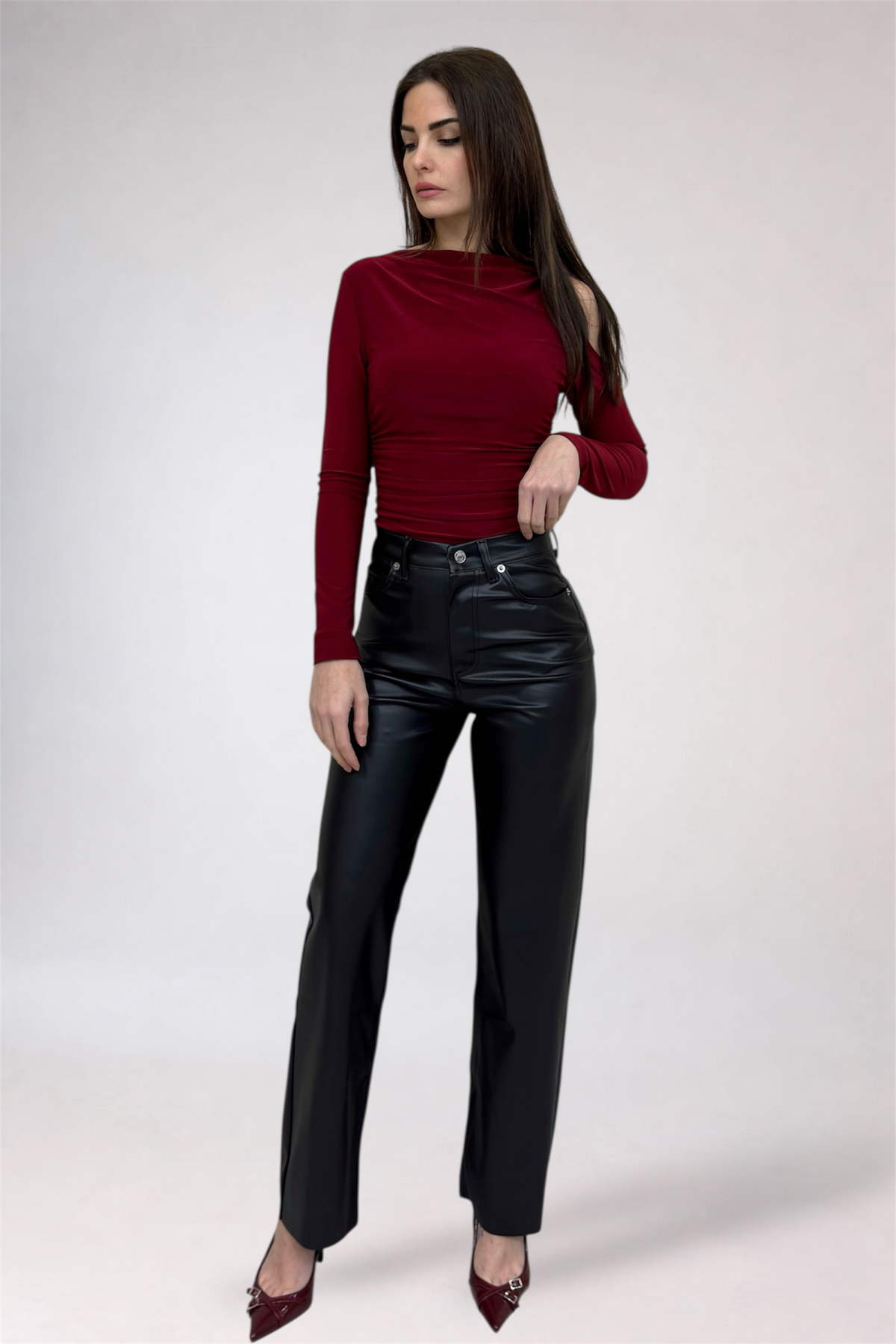 Woman wearing a red long-sleeve top and black leather pants on a white background