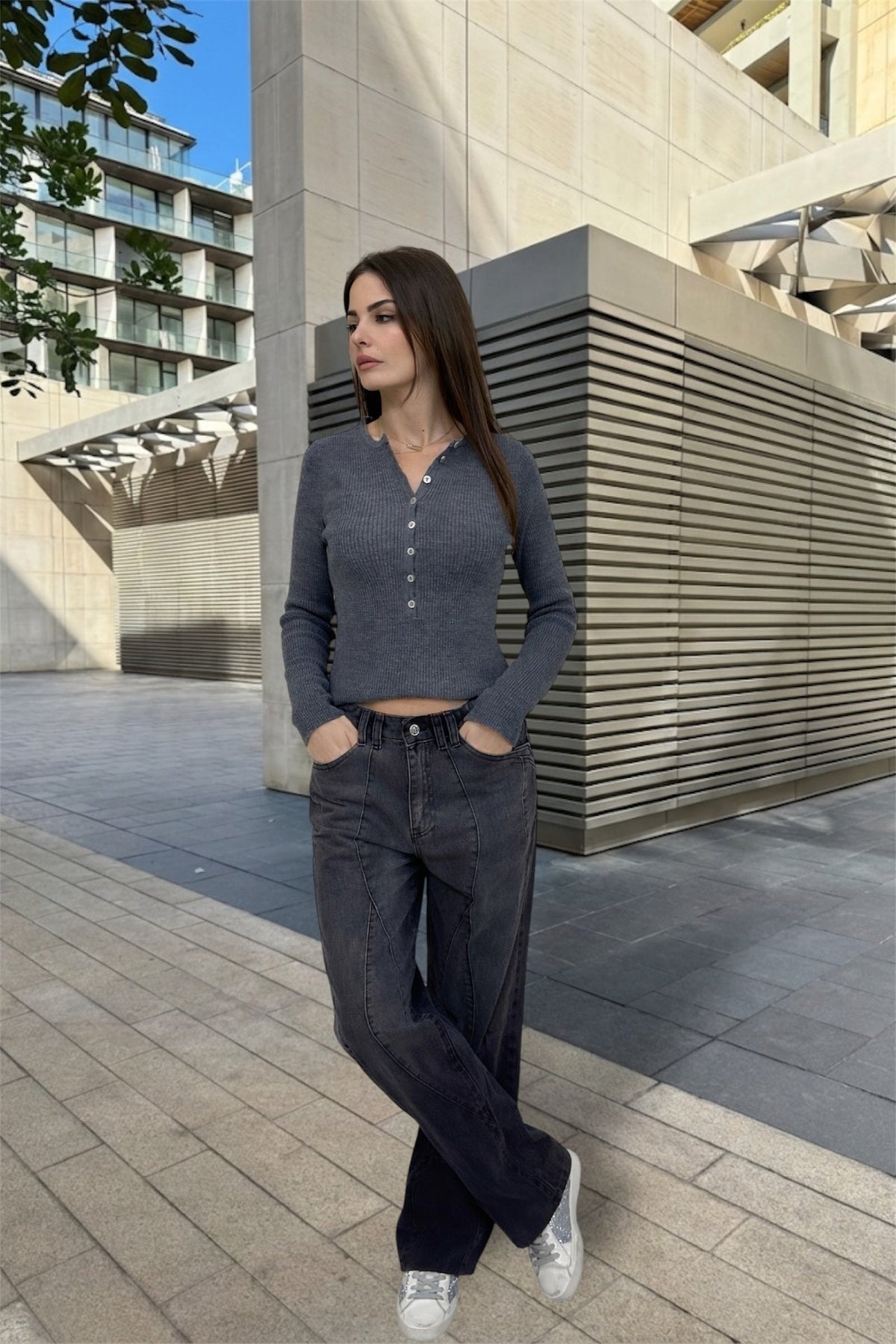 Woman in a gray outfit standing in an urban setting with modern buildings.