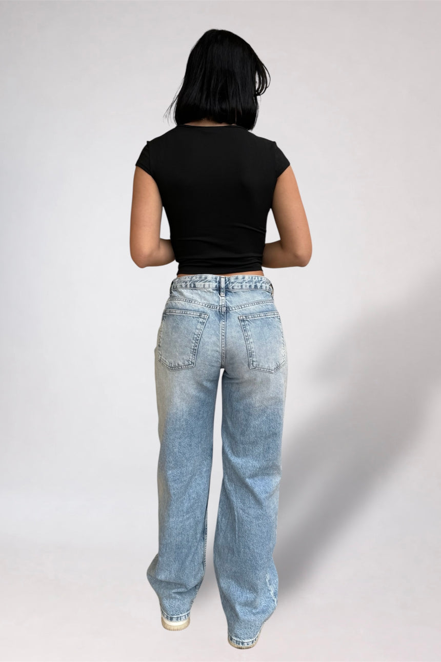 Person wearing a black t-shirt and light blue jeans on a white background