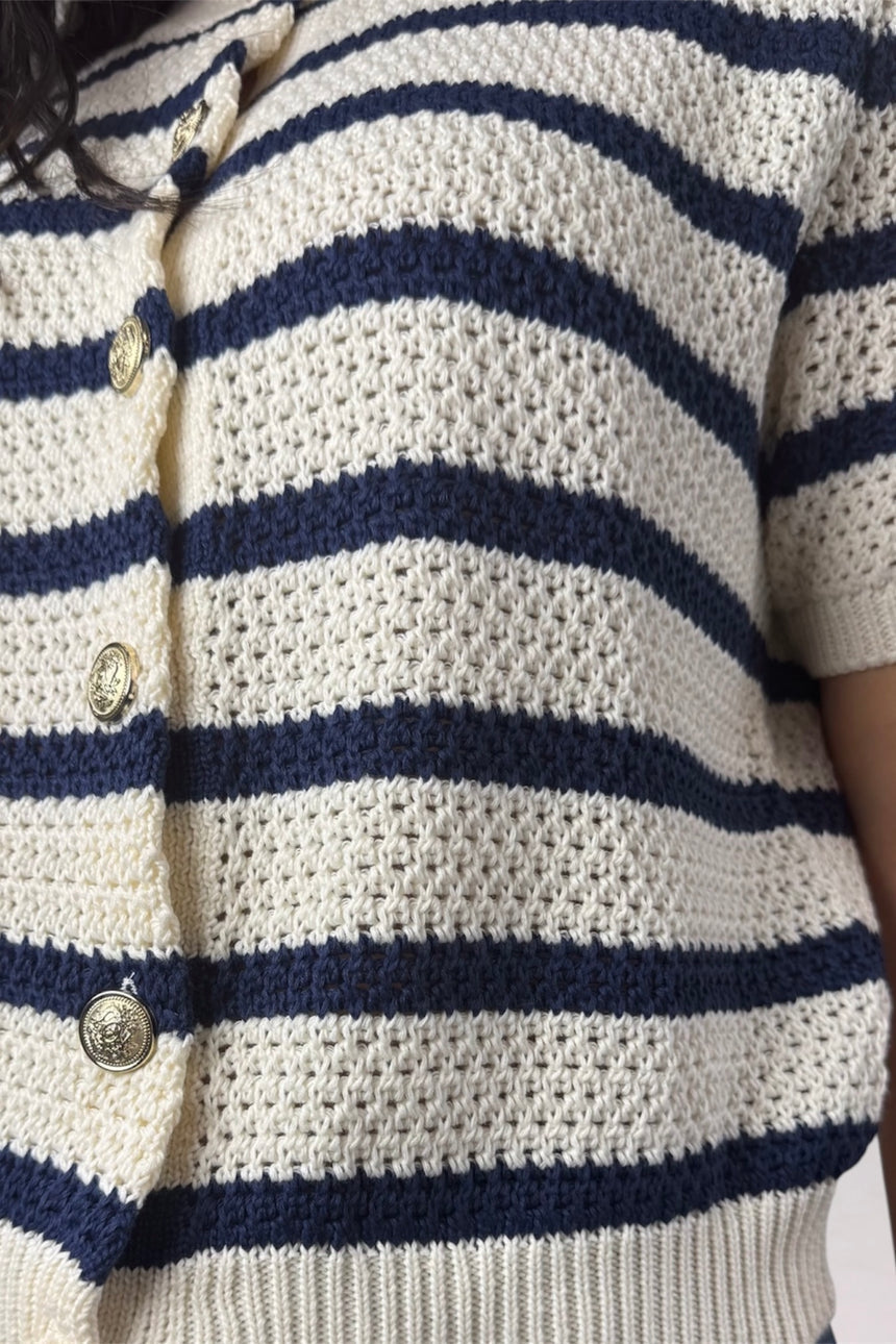 Close-up of a textured knit cardigan with horizontal navy blue and cream stripes, featuring a button closure with round gold-toned buttons.