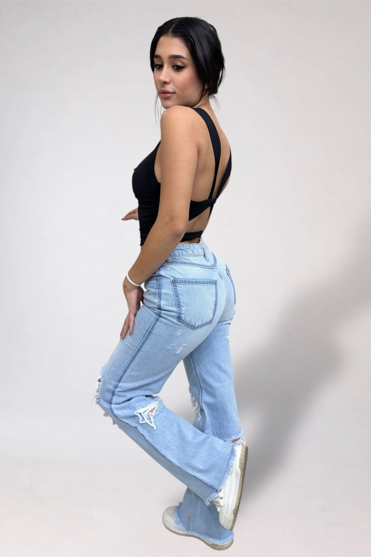 Woman wearing light blue jeans and a black top on a white background