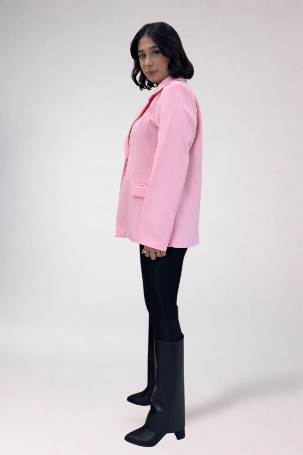 Person wearing a pink blazer, black pants, and black knee-high boots on a white background