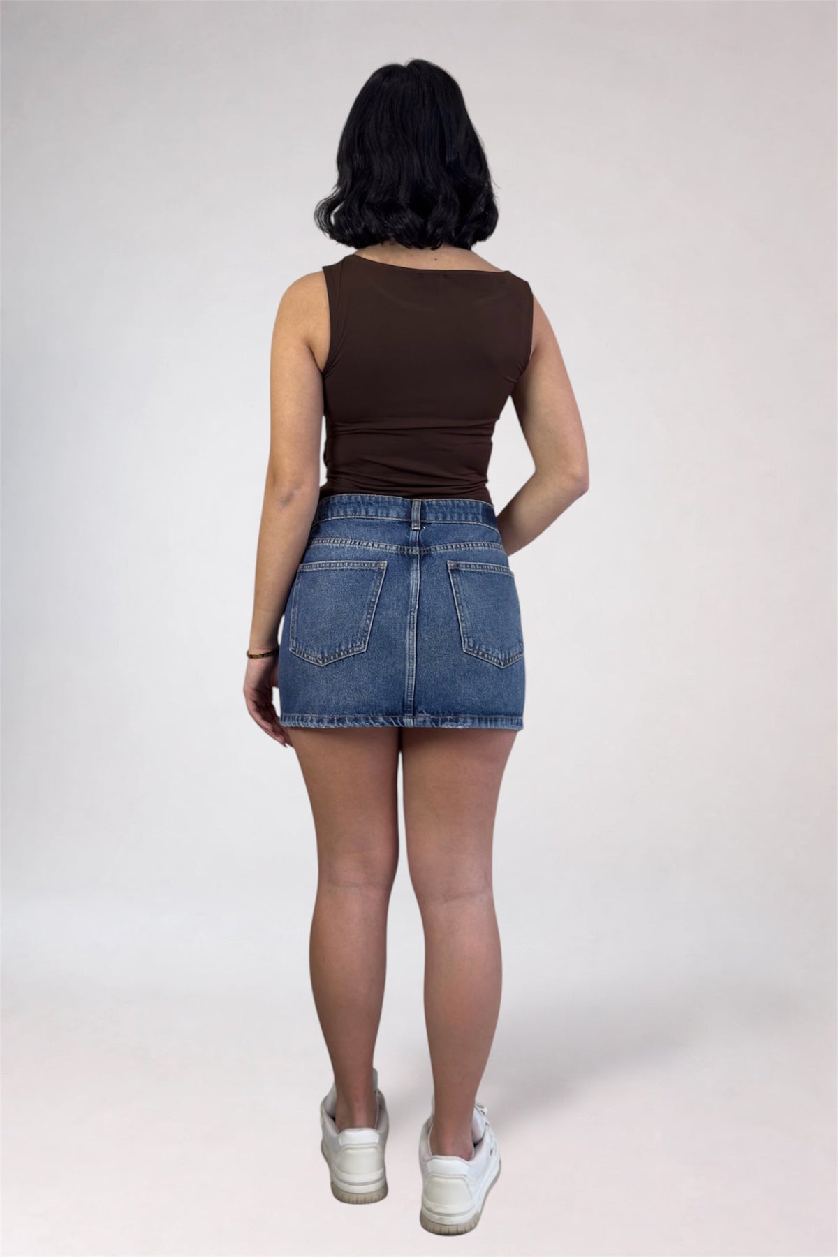Person wearing a brown tank top and denim skirt on a white background
