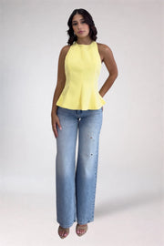 Woman wearing a yellow sleeveless top and blue jeans on a white background