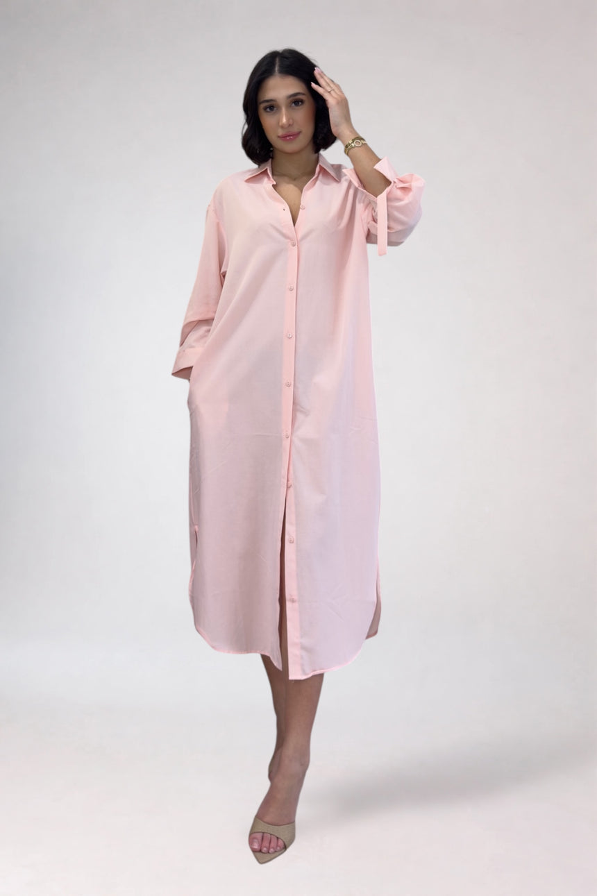Woman wearing a light pink shirt dress against a white background