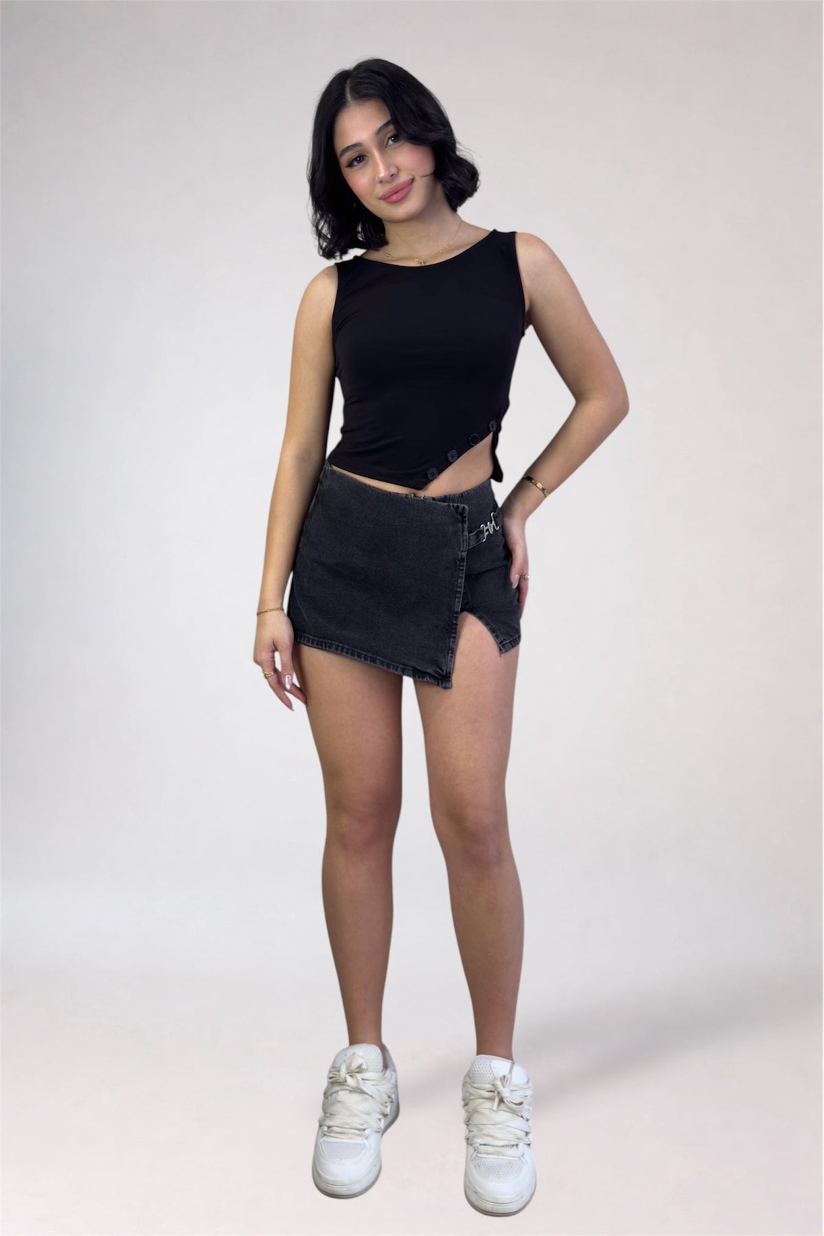Woman wearing a black sleeveless top and denim shorts on a white background