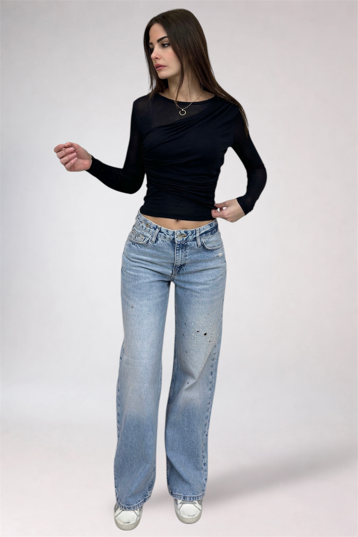 Woman wearing a black long-sleeve top and light blue jeans on a white background