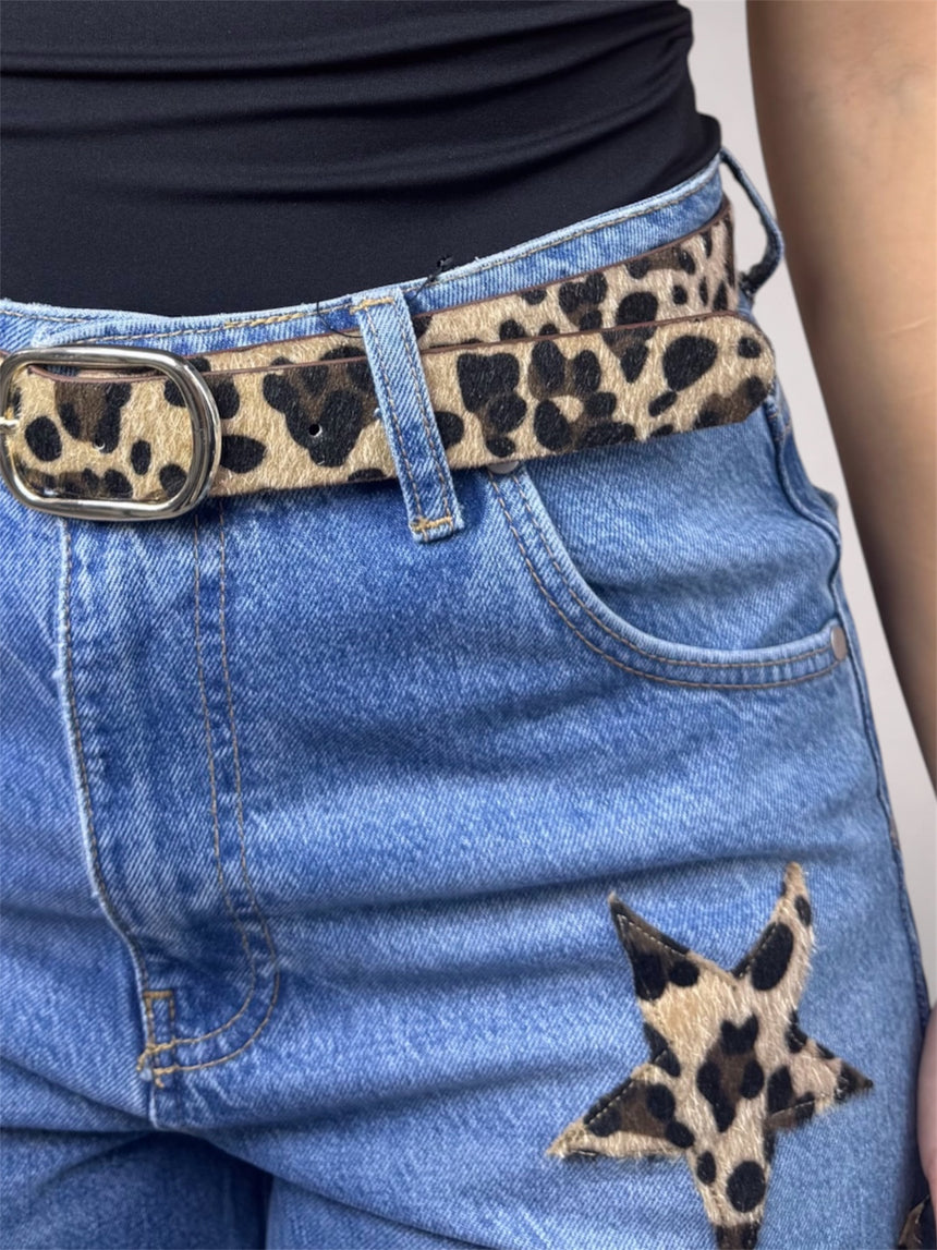 A close-up of a leopard print belt worn with blue denim shorts featuring a matching leopard star patch, paired with a black top.