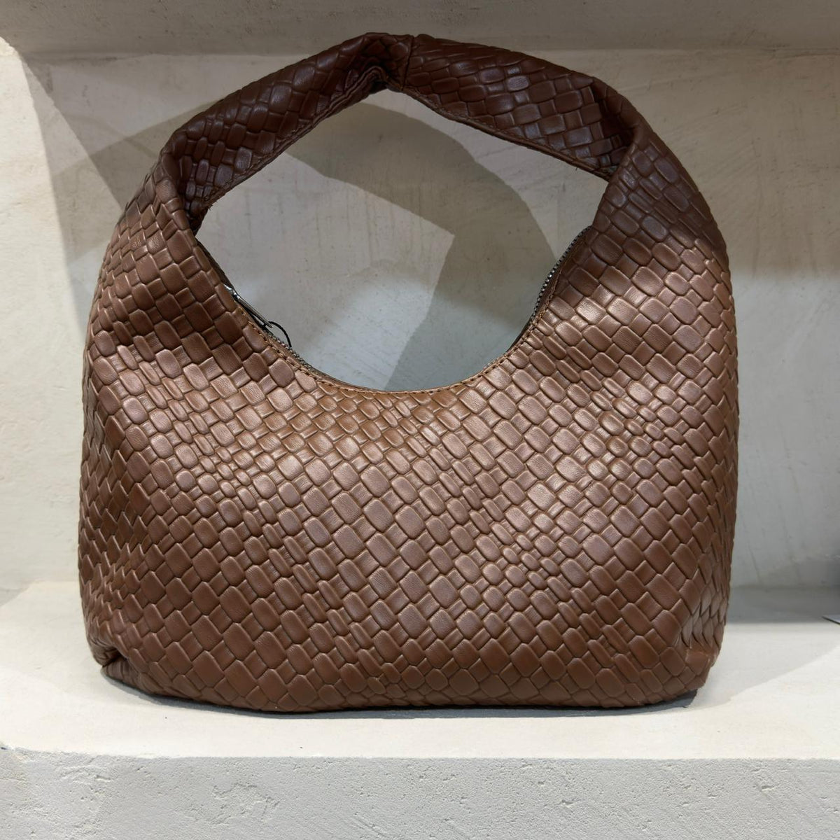 Brown woven handbag on a white surface with a light gray background