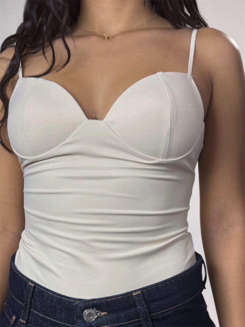 A close-up of a woman wearing a white ribbed camisole top with molded underwire cups and thin shoulder straps, paired with dark blue jeans.