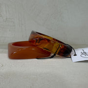 Amber-colored bracelet on a light gray surface with a visible brand tag.