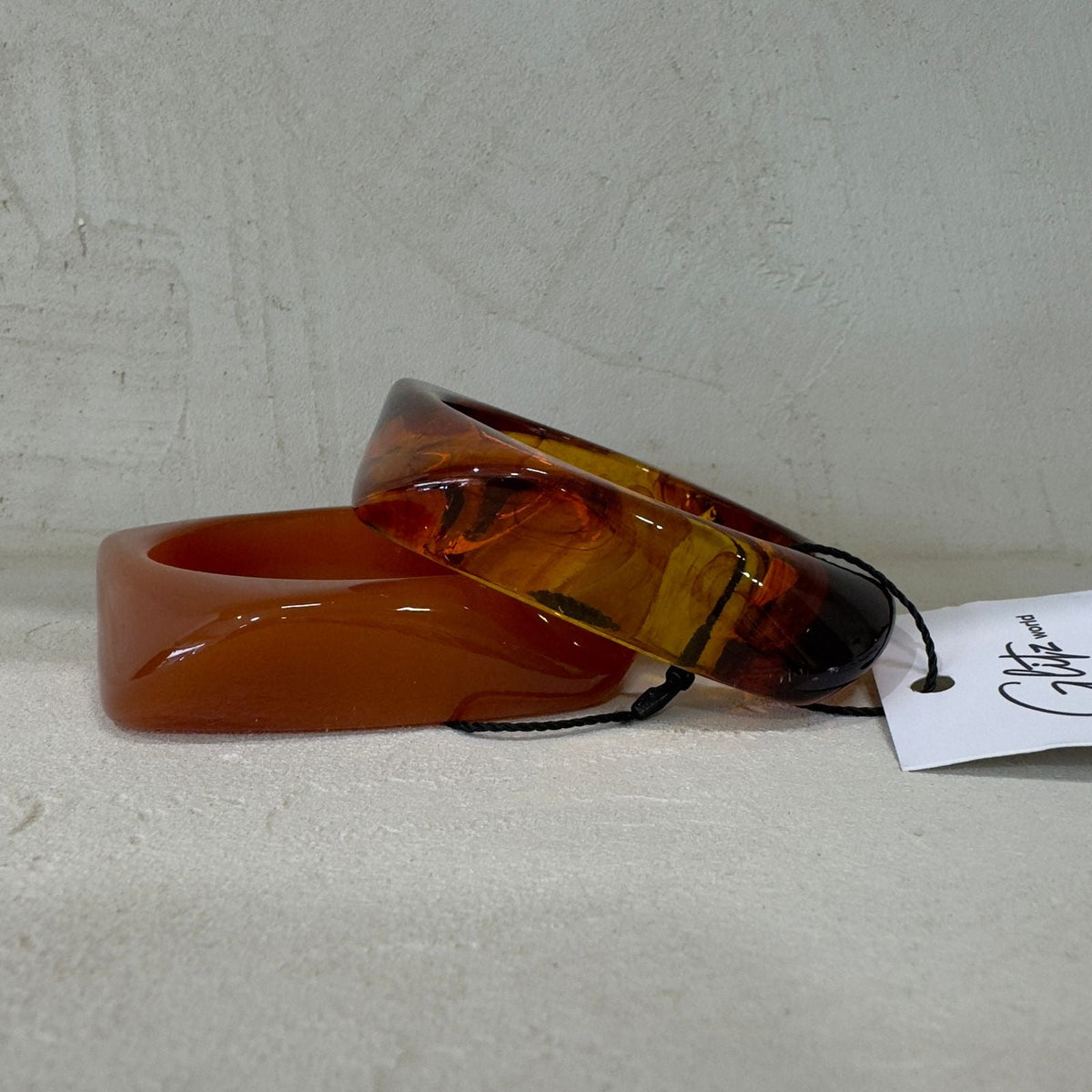 Amber-colored bracelet on a light gray surface with a visible brand tag.