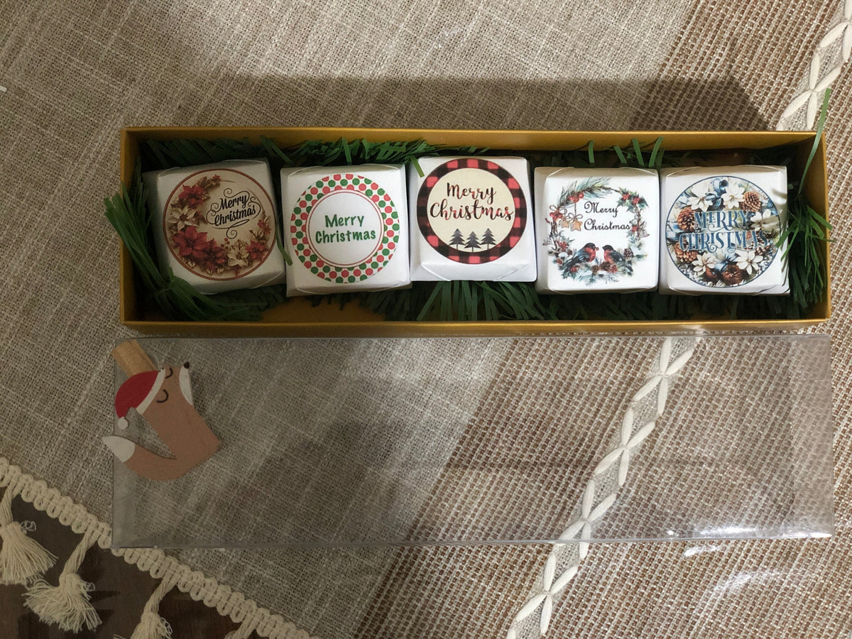 Set of five Christmas-themed coasters in a decorative box on a textured surface.