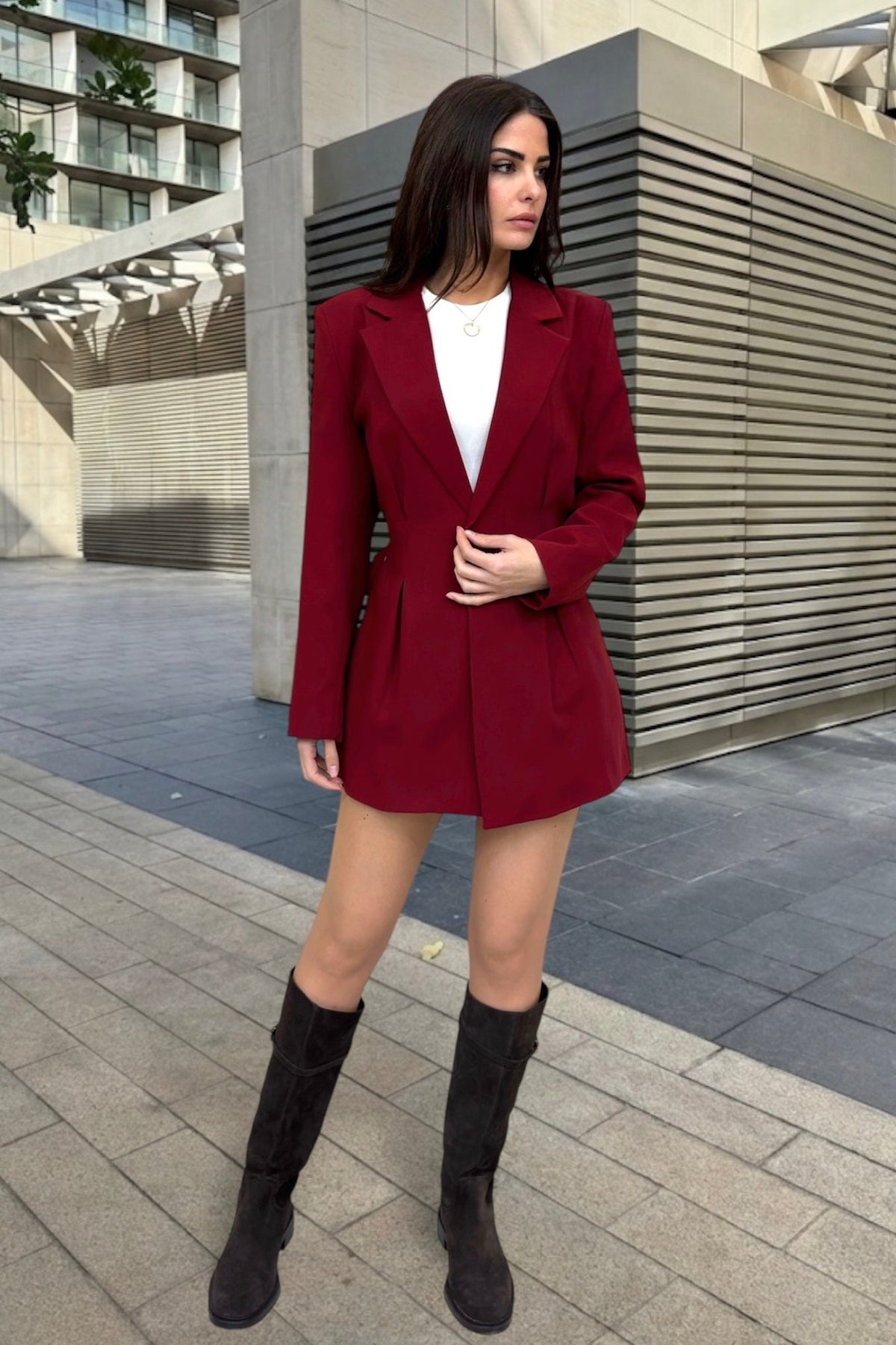 Woman wearing a red blazer and skirt set with black boots in an urban setting