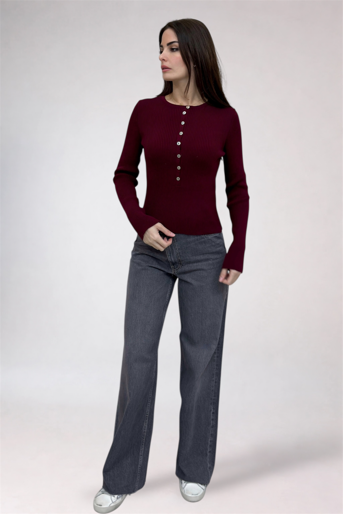 Woman wearing a burgundy long-sleeve top and gray pants on a white background