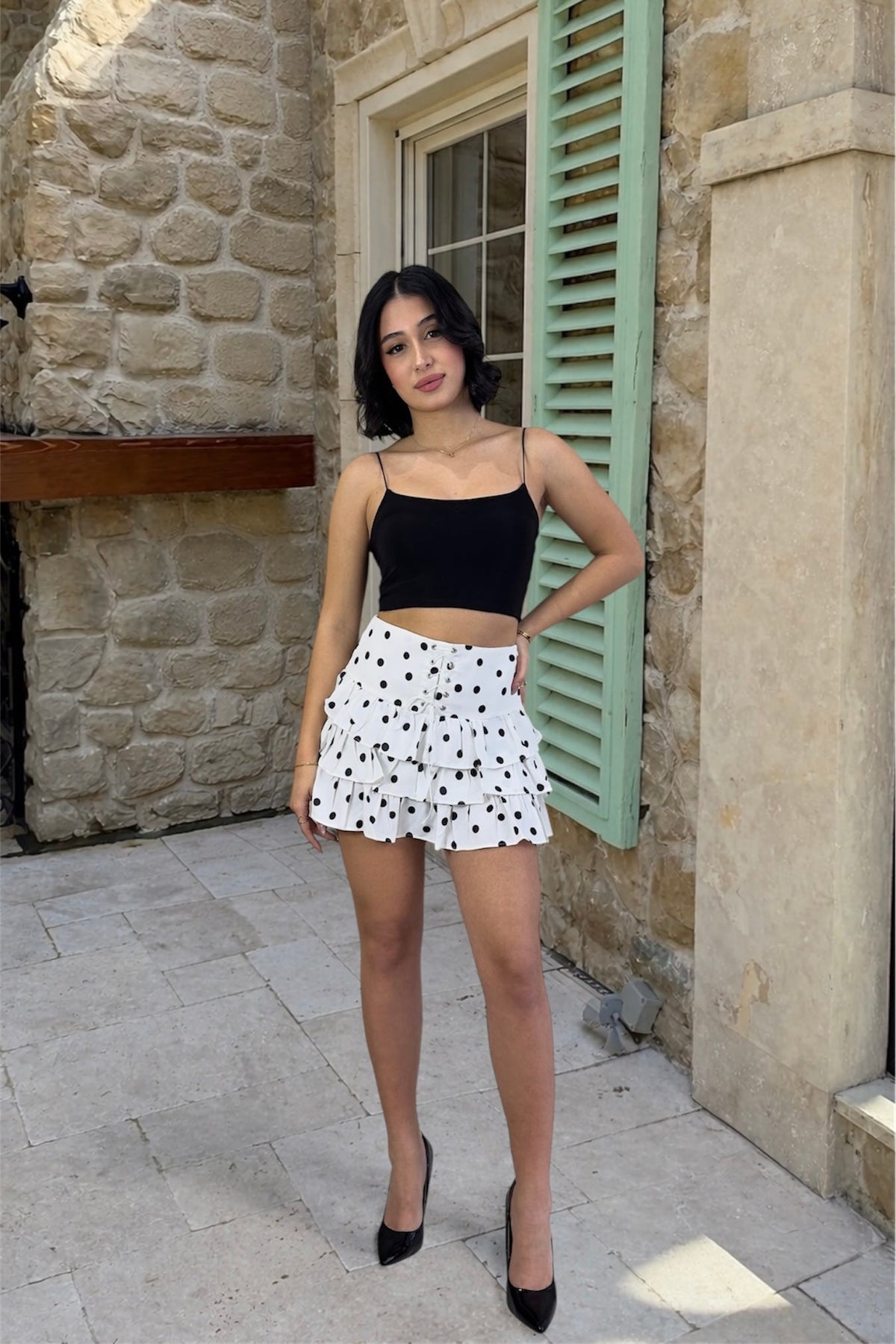 Woman in black top and polka dot skirt standing in front of a stone building.
