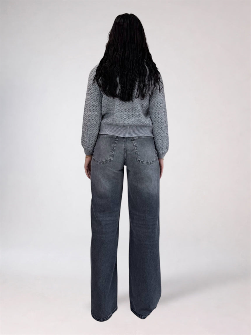 A person shown from the back wearing a gray textured knit sweater and wide-leg dark gray jeans against a plain light gray studio background.