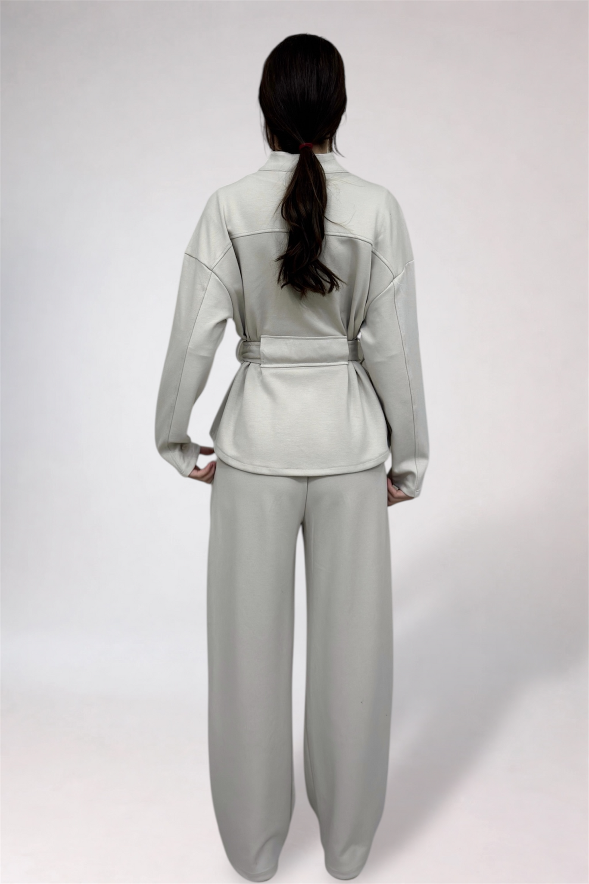 Person wearing a light gray outfit with a belt on a white background