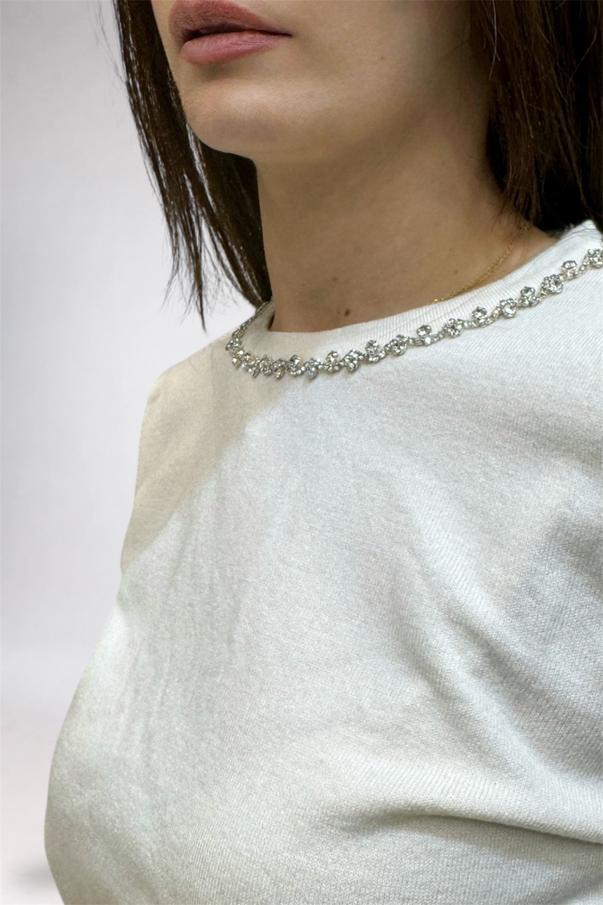 Close-up of a person wearing a white sweater and pearl necklace against a neutral background