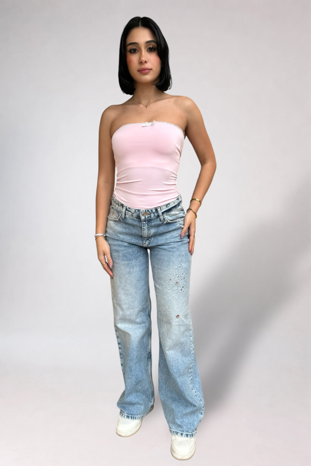 Woman wearing a pink strapless top and blue jeans on a plain background