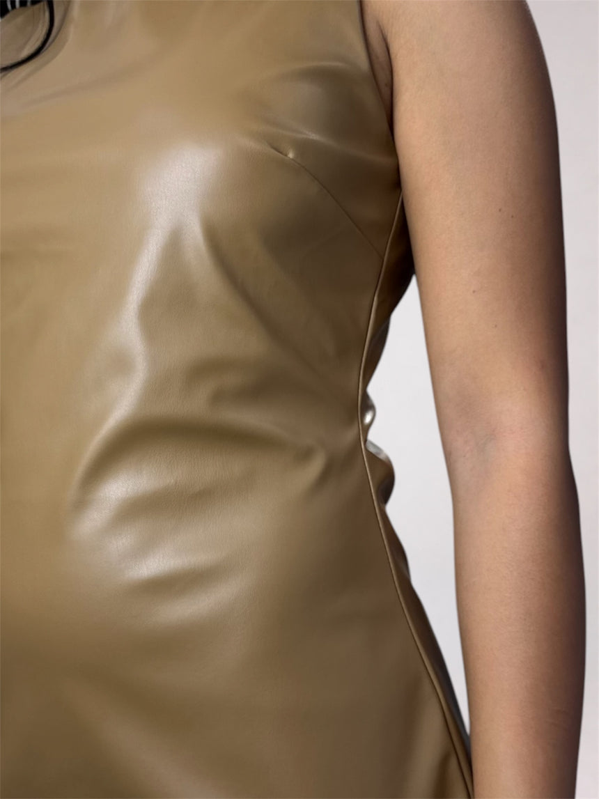 A woman modeling a sleeveless, bodycon mini dress in a shiny taupe-brown faux leather material, paired with black pointed-toe heels, against a plain light gray studio background.