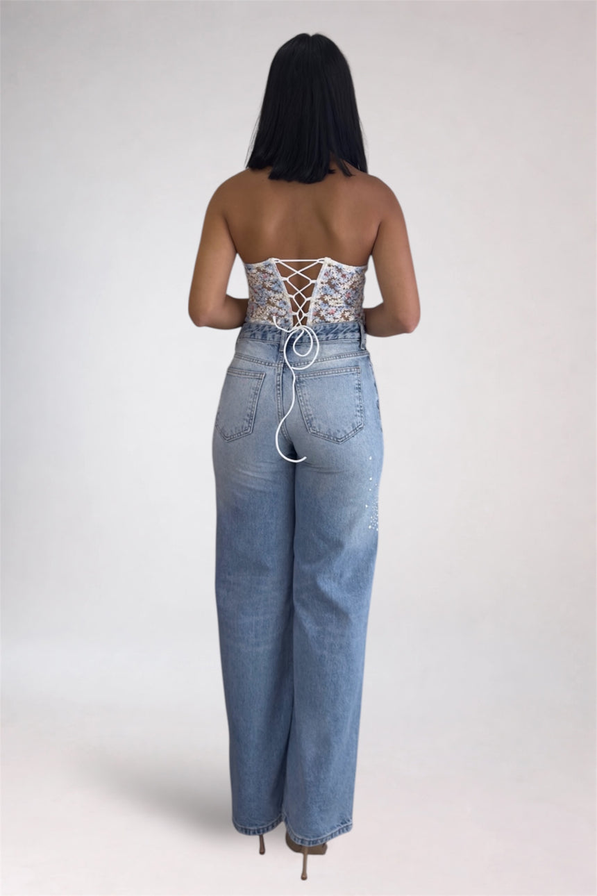 Woman wearing a strapless lace top and high-waisted jeans on a plain background