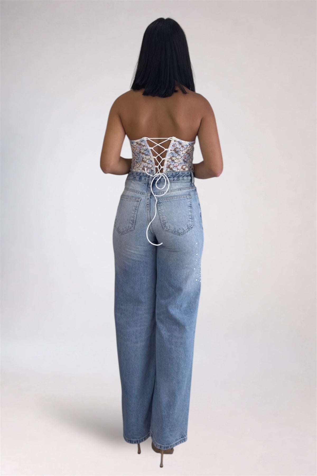 Woman wearing a strapless lace top and high-waisted jeans on a plain background
