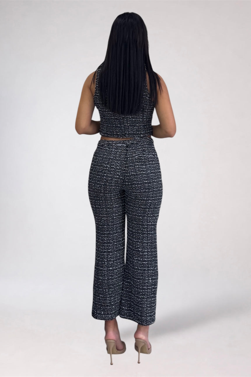 A woman viewed from behind wearing a matching sleeveless crop top and wide-leg pants set in a black and white textured tweed pattern, paired with beige high heels, against a light gray studio background.