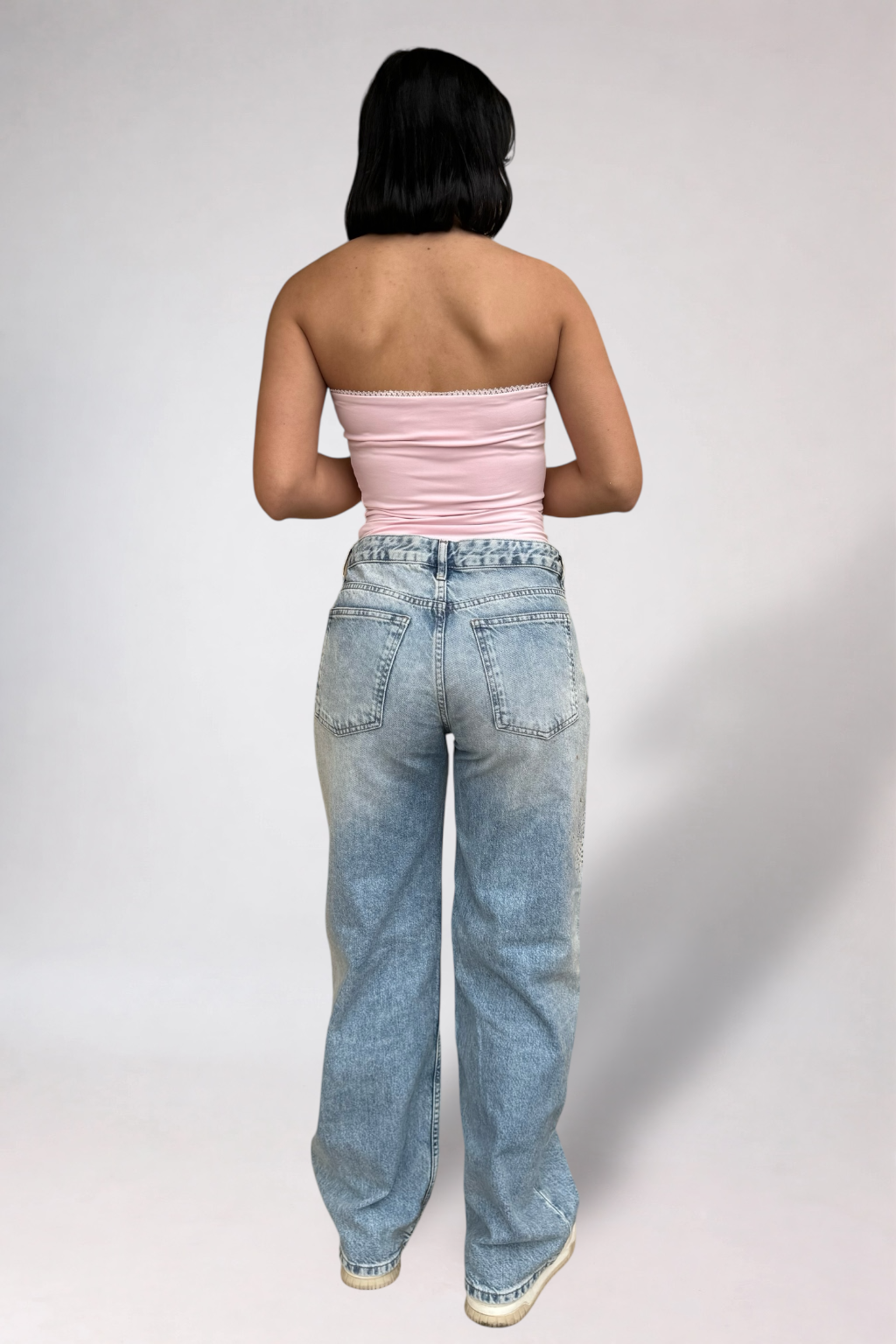 Person wearing a pink strapless top and blue jeans on a plain background