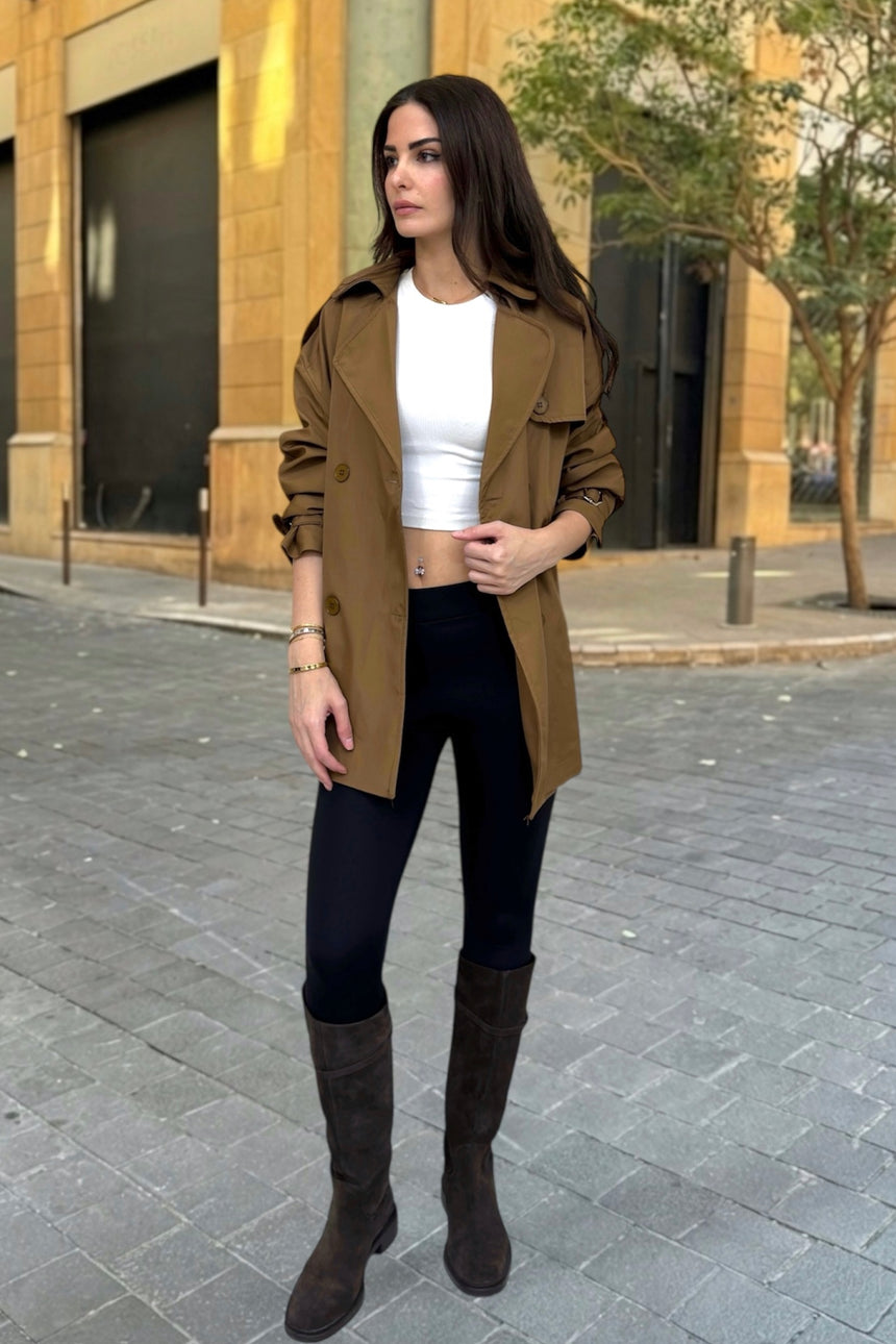 Woman wearing a brown coat, white top, black pants, and brown boots on a city street.