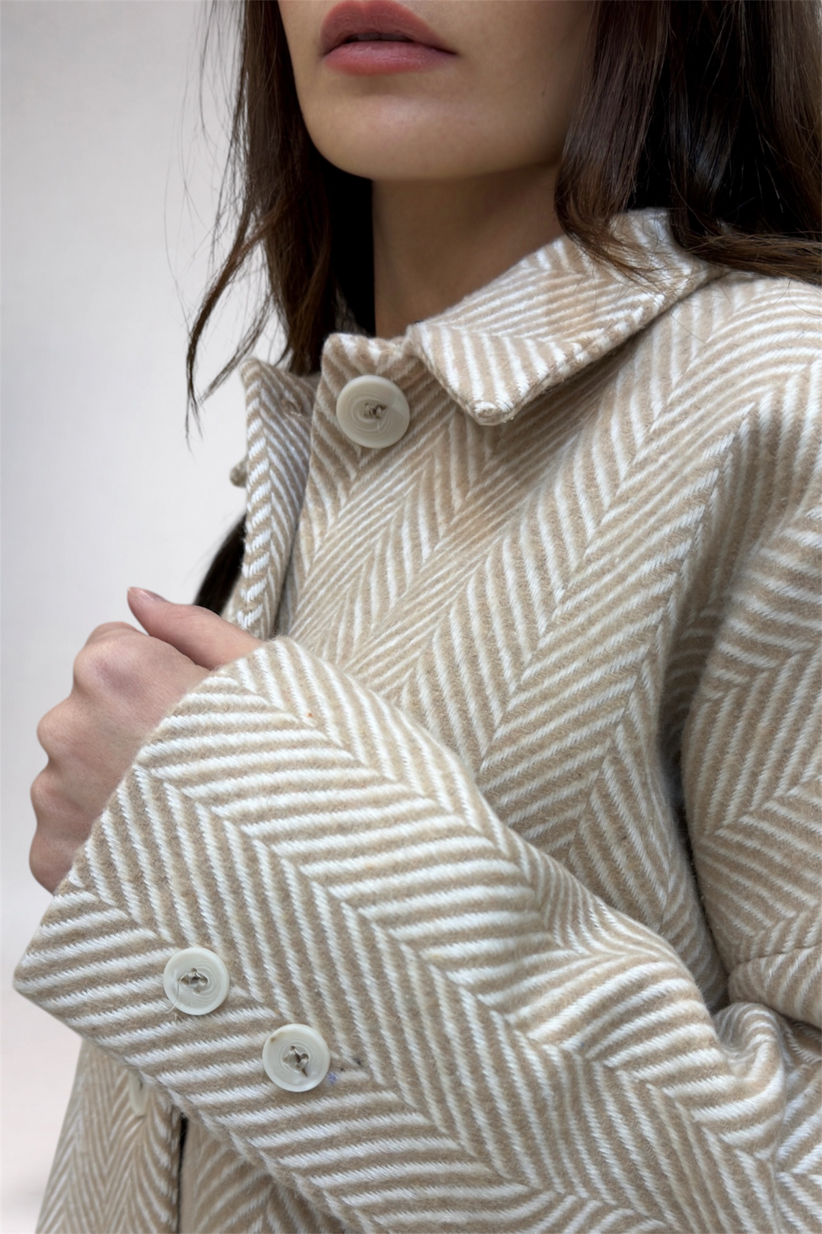 Close-up of a person wearing a herringbone patterned coat with a neutral background