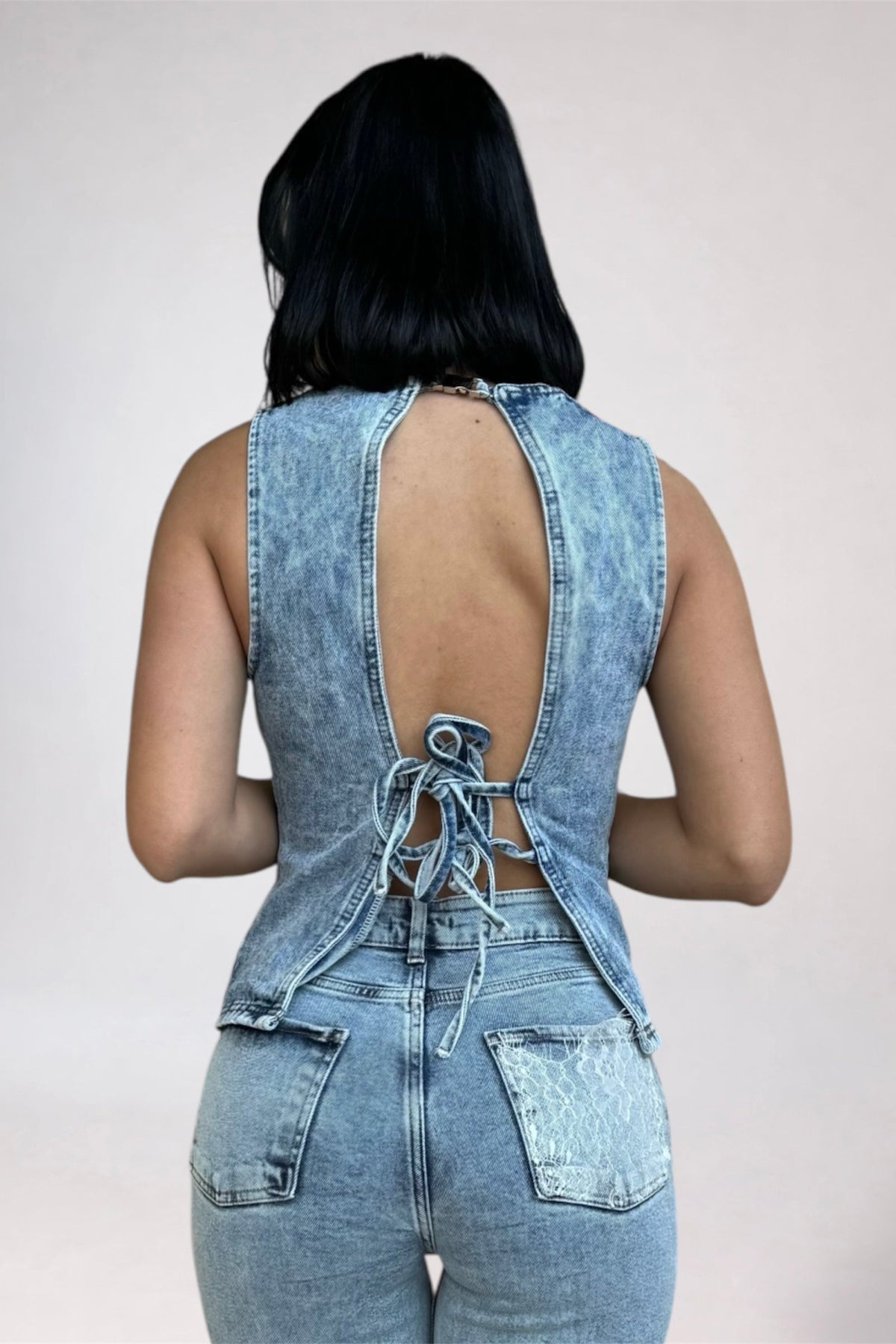 Person wearing a denim jumpsuit with an open back on a plain background