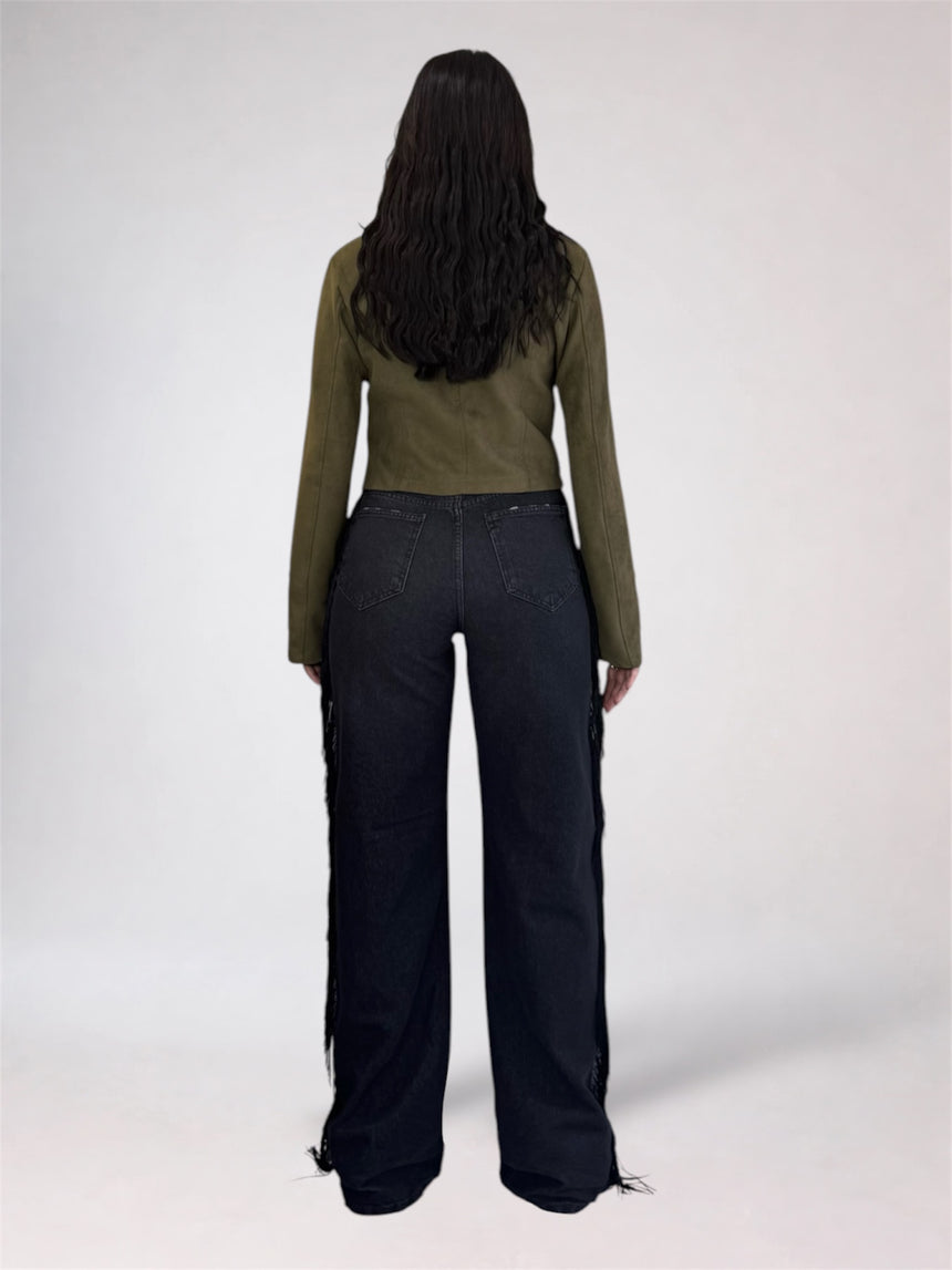 A model shown from the back wearing an olive green long-sleeve top and dark wide-leg jeans with fringe detailing along the outer sides, set against a plain light gray studio background.
