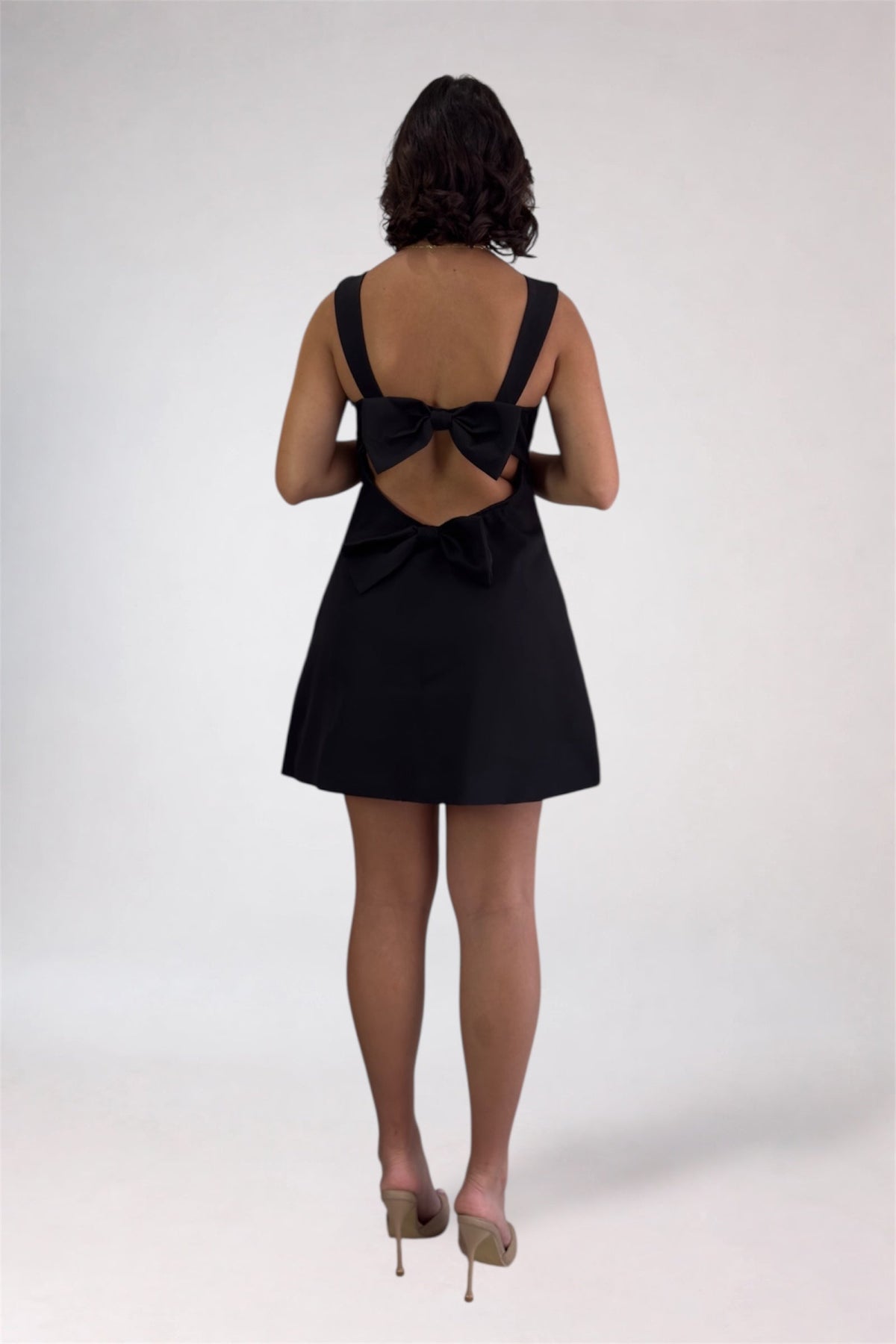 Black dress with a bow detail on the back worn by a person on a white background
